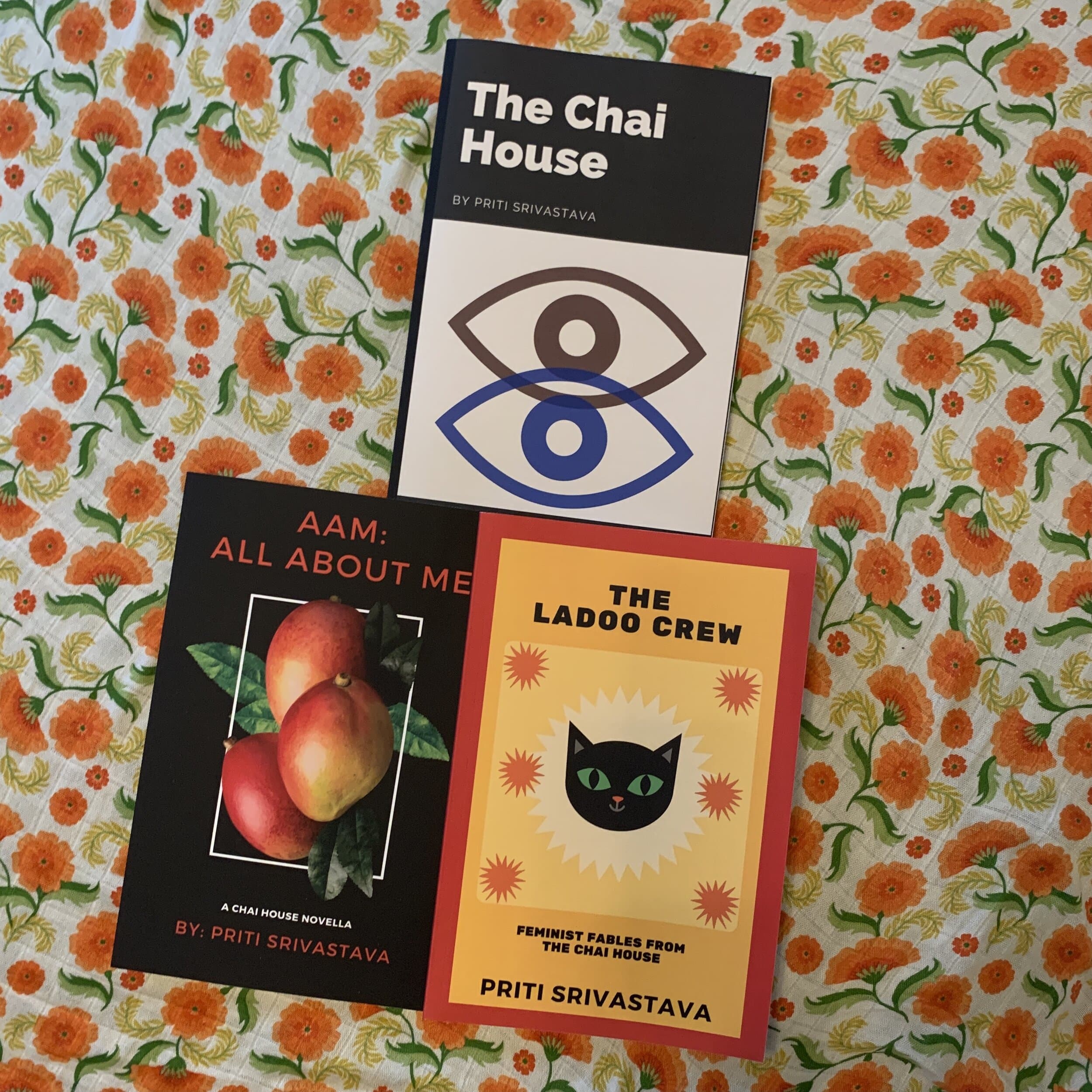 “The Chai House,” “AAM: All About Me,” and “The Ladoo Crew” books are set on a patterned background of bright orange flowers.