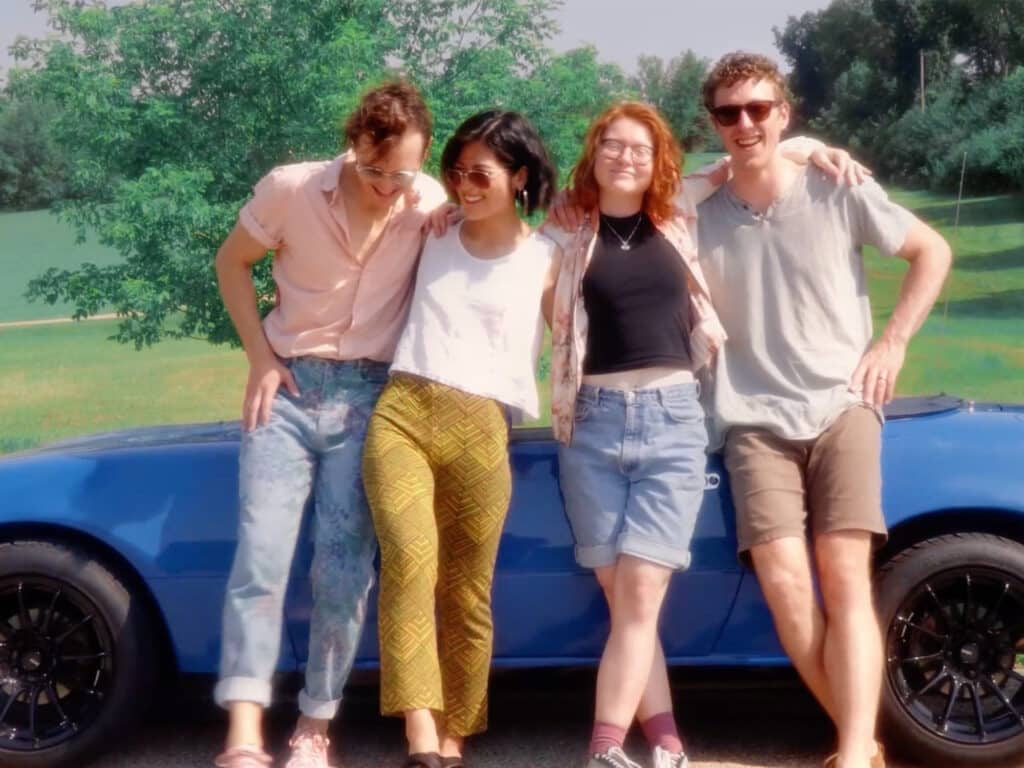 The four members of LINE are shown leaning against a blue convertible.