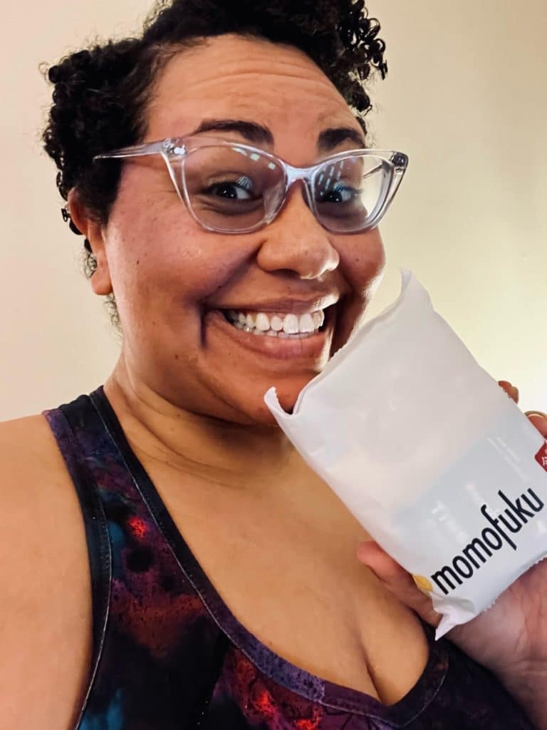 The author is shown in a selfie, smiling at the camera and holding up a packet of noodles with the word "Momofuku" printed on it.