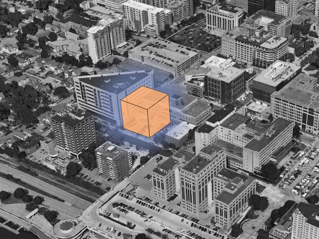 An illustration shows a bird's-eye view of several blocks of downtown Madison in black and white. Superimposed upon it is an orange cube that shows the site of a proposed new jail building.