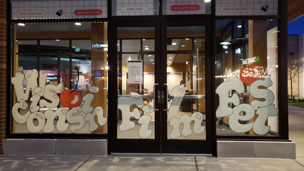 A nighttime photo outside the main entrance to Wisconsin Film Festival Hilldale shows window decal art in the decadent visual theme with cherries. Photo by Grant Phipps.