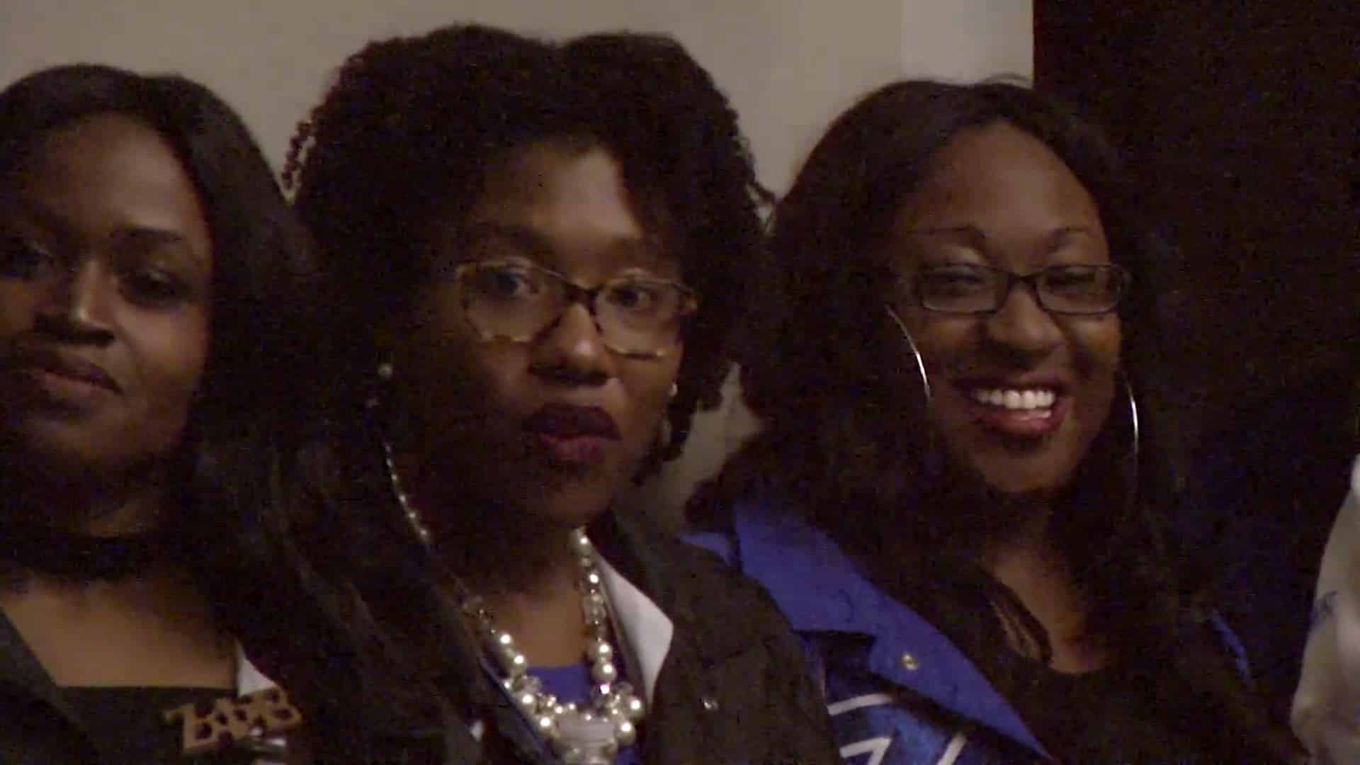 Three Black women turn their gaze towards a camera filming an event at Tau Theta Chapter of Zeta Phi Beta.