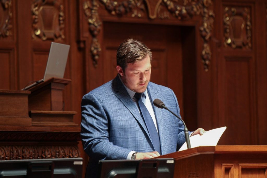 Photo image of Rep. Clinton Anderson in a blue suit speaking at a podium. 