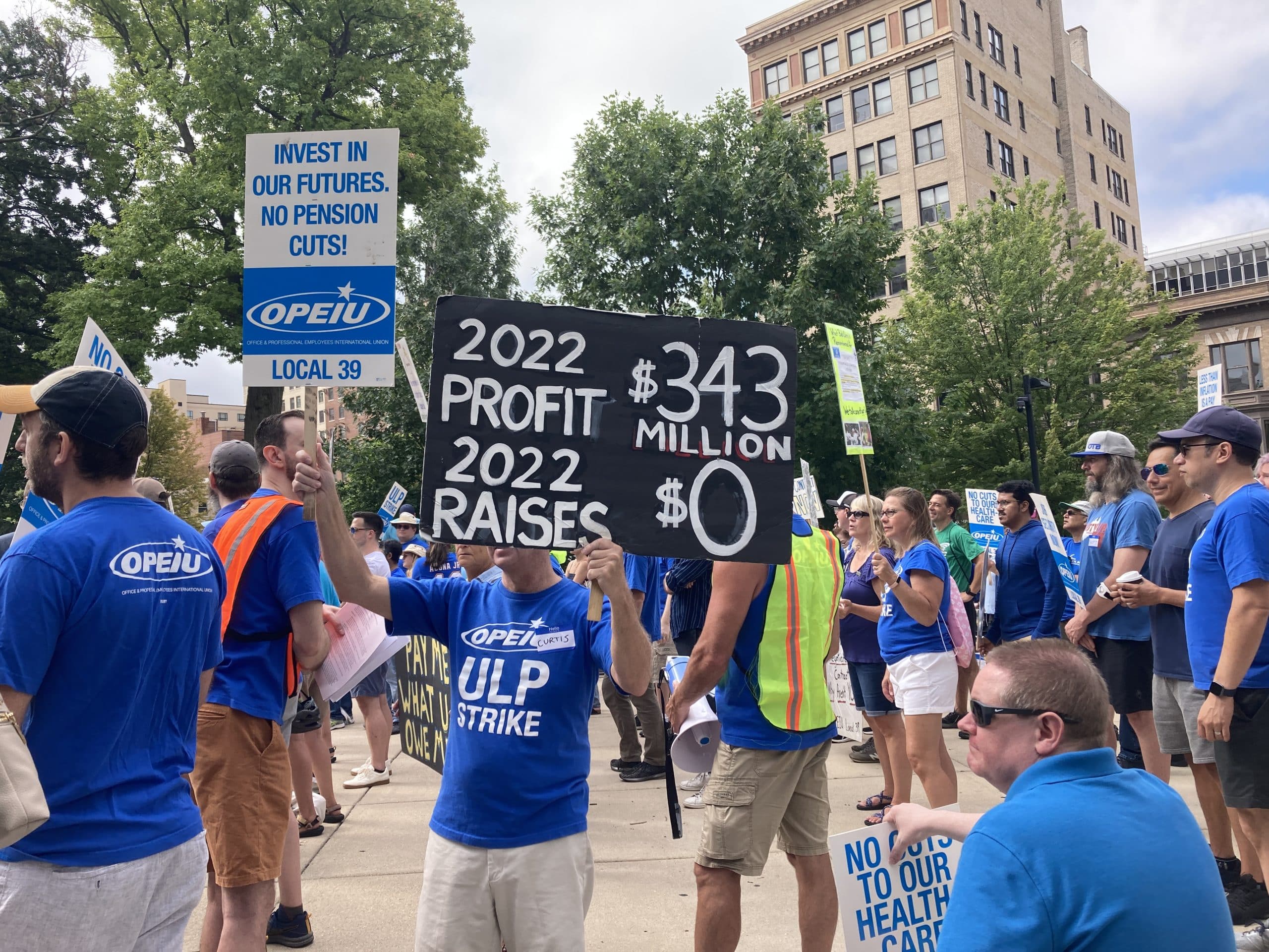 Photo of a crowd of workers on Capitol Square wearing blue union shirts and carrying signs. A sign in the foreground reads, "2022 profit: $343 million. 2022 raises: $0."
