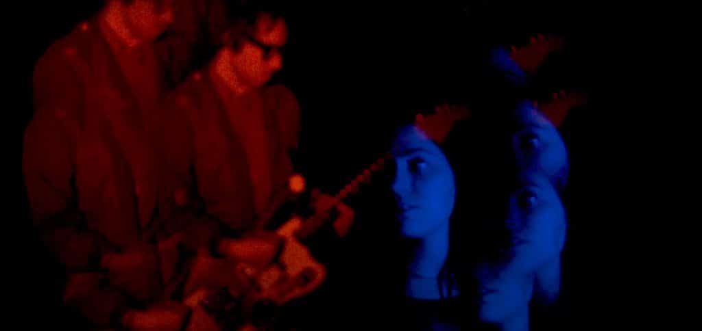 A still from the music video for "Convene" shows an image of guitarist/vocalist Ronnie Lee bathed in reds, and depicted in multiple overlays on the left hand side, while his creative and romantic partner, bassist/vocalist Hannah Porter is shown in blues on the right hand side, also in multiple overlays. Porter's looking to the left of the screen, while Lee is shown playing a Fender Jazzmaster, his head down.