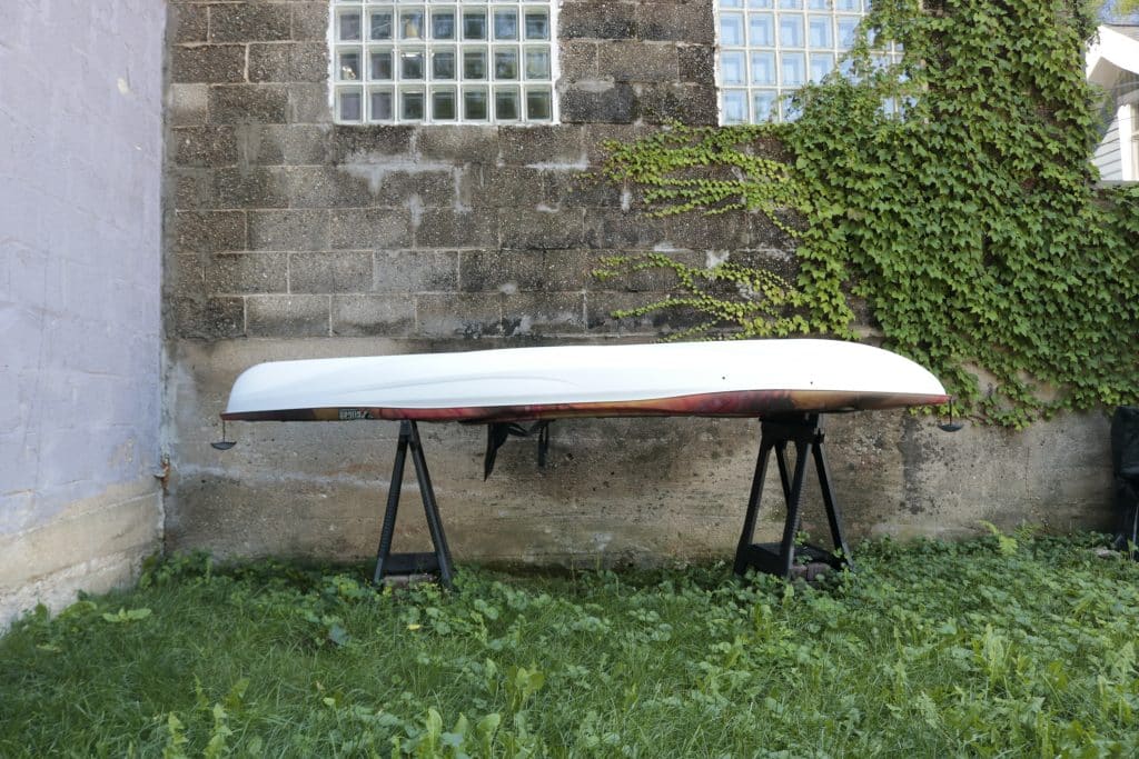 A white kayak rests upside down on saddle horses in the grass by a stone building.
