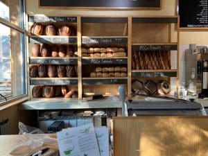 A photo of a bakery with a wall full of different types of bread behind the counter.