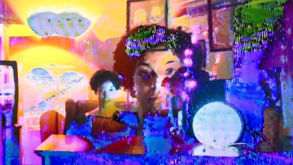 An image distorted in splotches of neon yellow and pink light halos gradually turning to blue, purple, and green also displays a woman (Bianca Martin) sitting and staring at the camera. Her mirror image is projected larger to her right. The negative image of a crystal ball rests below her to the right of that.