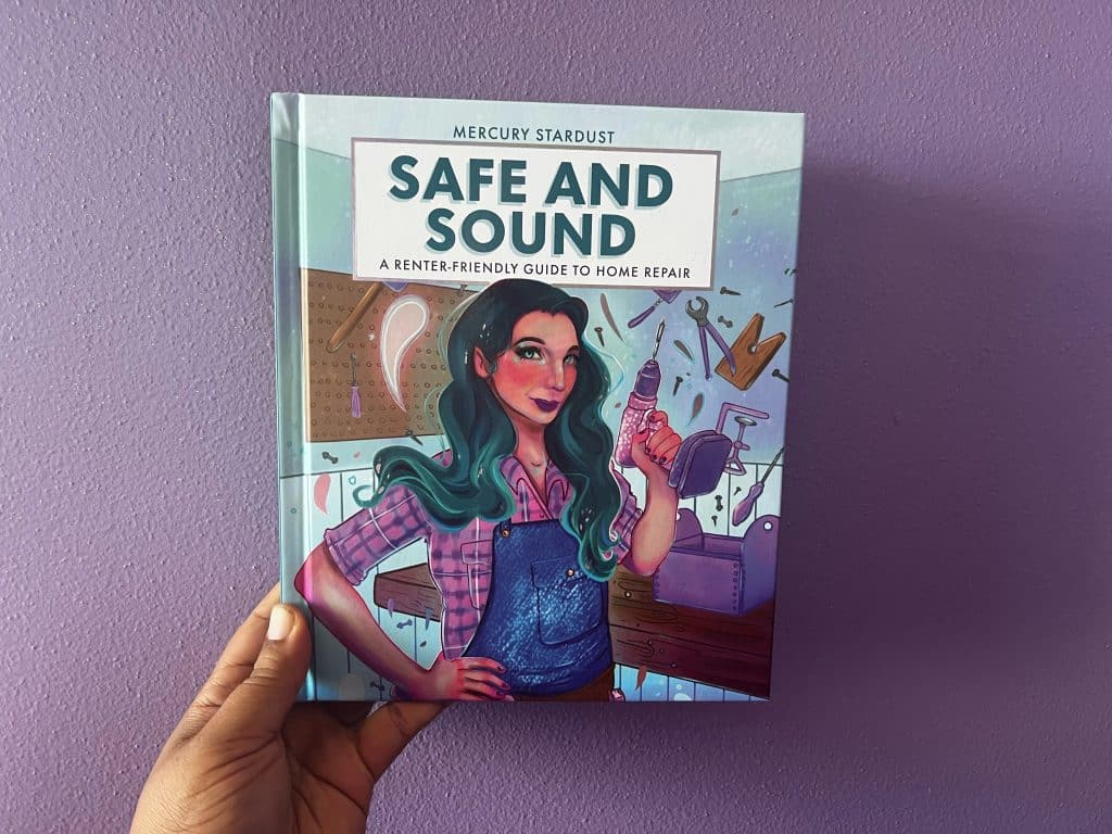 Sami Schalk holds Mercury Stardust's hardcover book up against a lavender-colored wall.