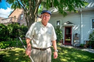 A man stands outside a house with his cane.
