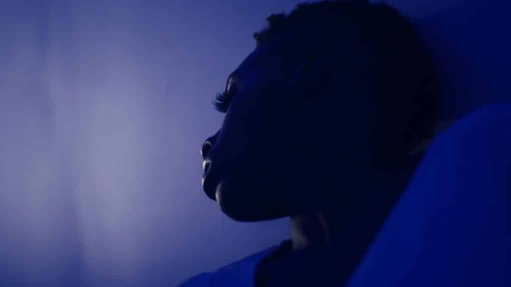 A low-angled close-up of a Black woman (dancer Bianca Melidor) in a stylized profile in the film "Quiet As It's Kept." She is captured in a color gradient of midnight blue.