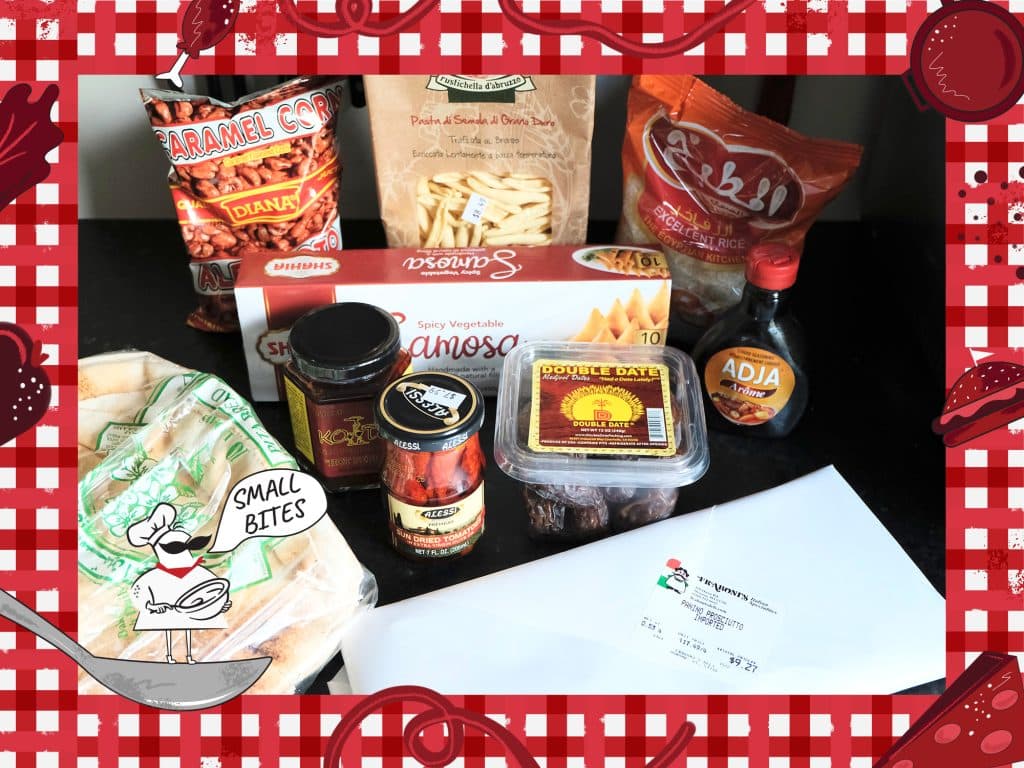 A selection of packaged, bottled, and jarred food items from the Italian market, Fraboni's, as well as pan-African grocery store, Gooh Grocery, sit on a black countertop. Items include caramel corn, imported pasta, samosas, dates, sun-dried tomatoes, and prosciutto. An illustrated frame around the photo depicts a checked tablecloth pattern with various items of food. In the bottom left corner, a small caricature chef stands on a spoon with the speech bubble, "Small Bites."