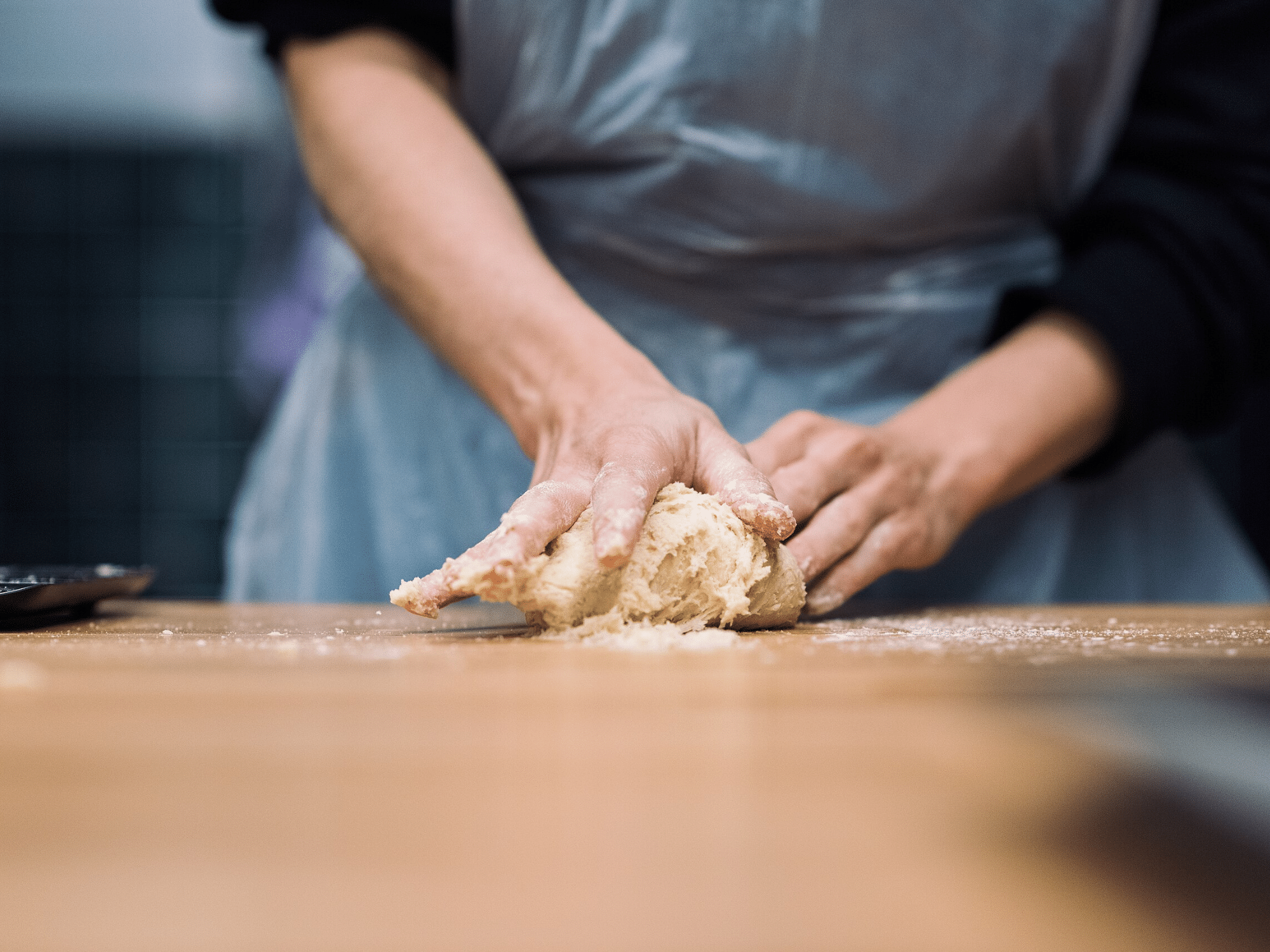 Photo of bread being kneaded by hand on a wooden table.