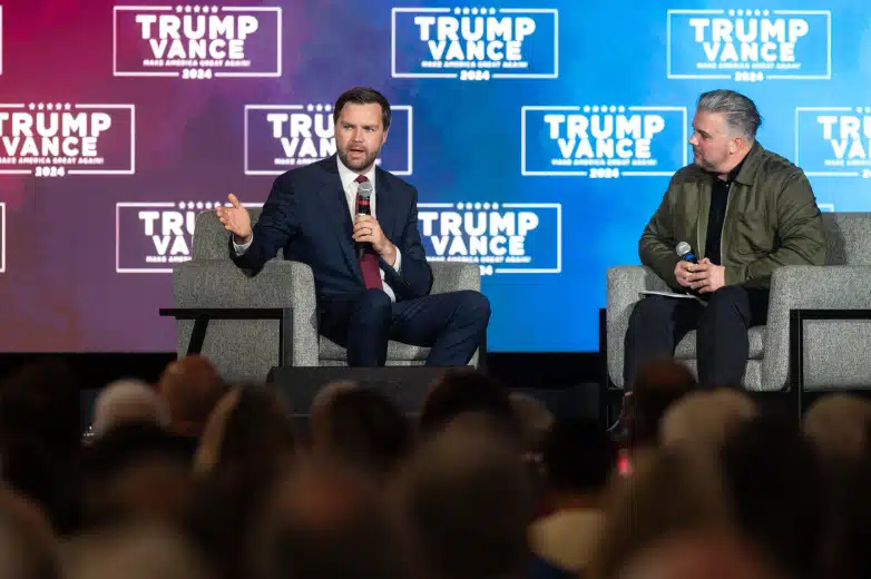 Vice Presidential candidate JD Vance speaks seated on a stage while Jason Howard listens.