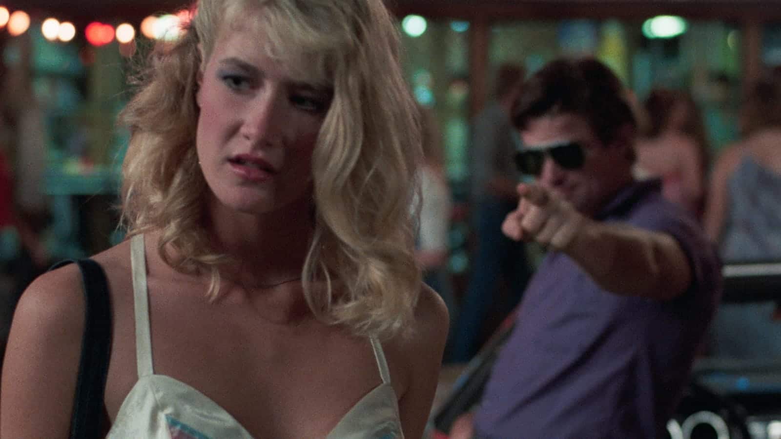 Teenage Connie Wyatt (Laura Dern) stands in the foreground at a close-up. She wears a white halter top and has a perturbed expression. Behind her, slightly out of focus, an older man (Treat Williams) in sunglasses and a purple shirt points threateningly.