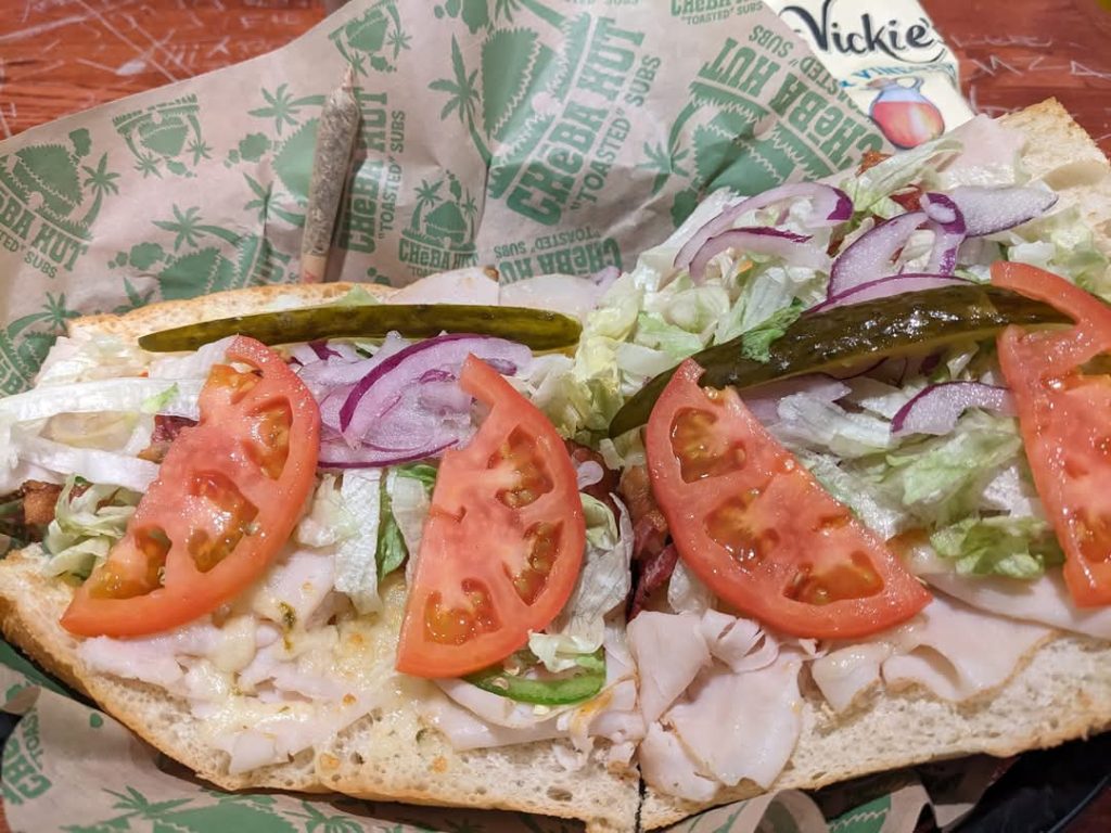 Close-up photo of an open-faced sub sandwich with numerous toppings, including lettuce, red onions, tomatoes, and pickles.
