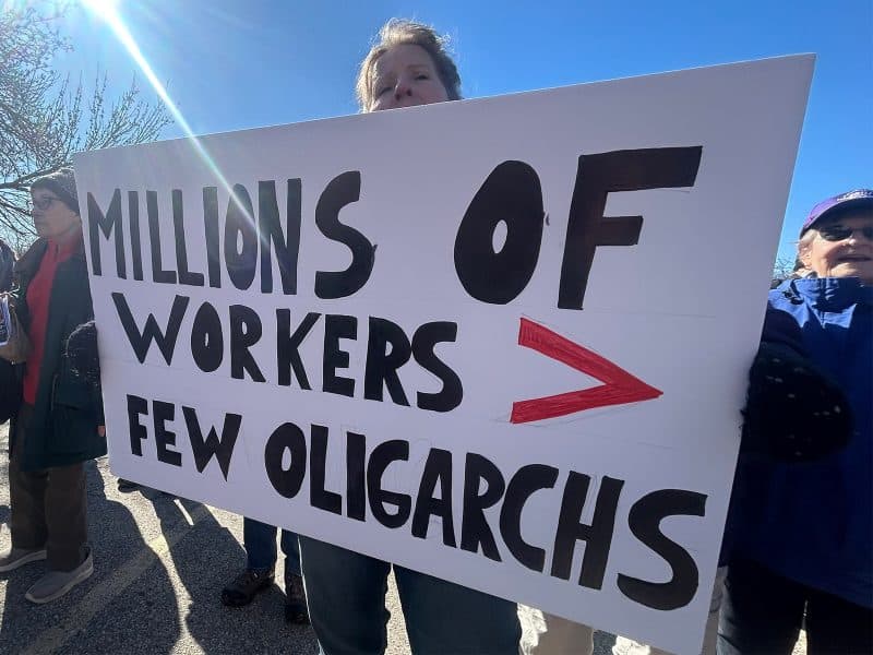 A woman holds an anti-billionaire sign at a rally outside of Madison's Labor Temple on March 22. The sign reads "Millions of workers > few oligarchs."
