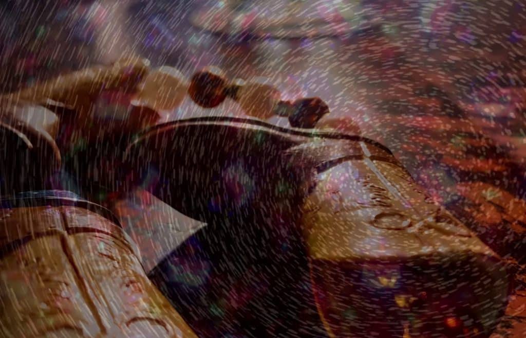 Superimposed images create a psychedelic effect in a still from "Honky Tonk Angels." In the foreground, a glass-bead necklace is threaded with plastic cowboy boots. The necklace is laying flat on a surface with an ambiguous print pattern with one of the boots nearly centered in the frame. A night sky-like pattern spinning in mid-motion is overlaid on top.