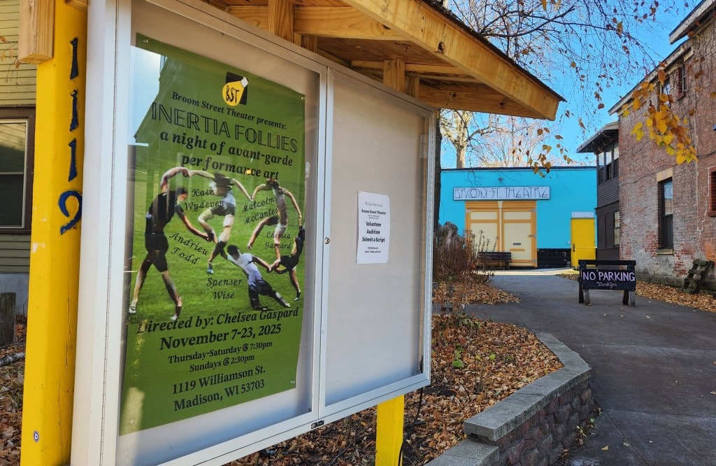 Autumn season photograph of the cased bulletin board in front of Broom Street Theater in Madison at 1119 Williamson Street. The case displays the predominantly forest green-colored show poster with information about