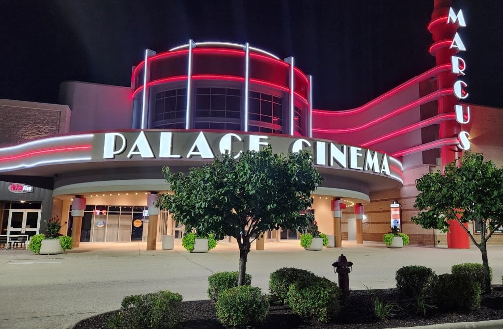 Photo taken from the parking lot of a neon-lit movie theater entrance that says 