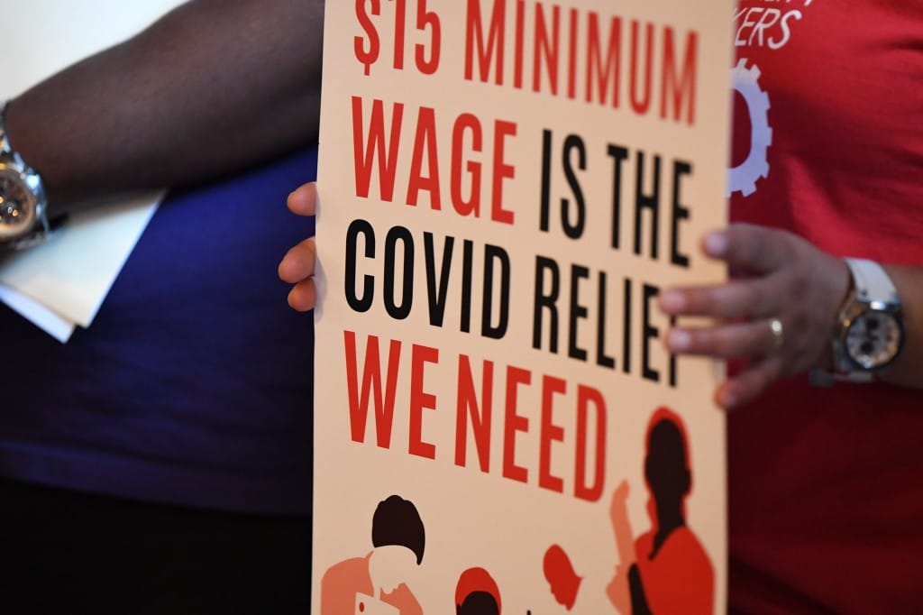 Slightly angled close-up photo of a person holding a sign with two hands. The sign reads