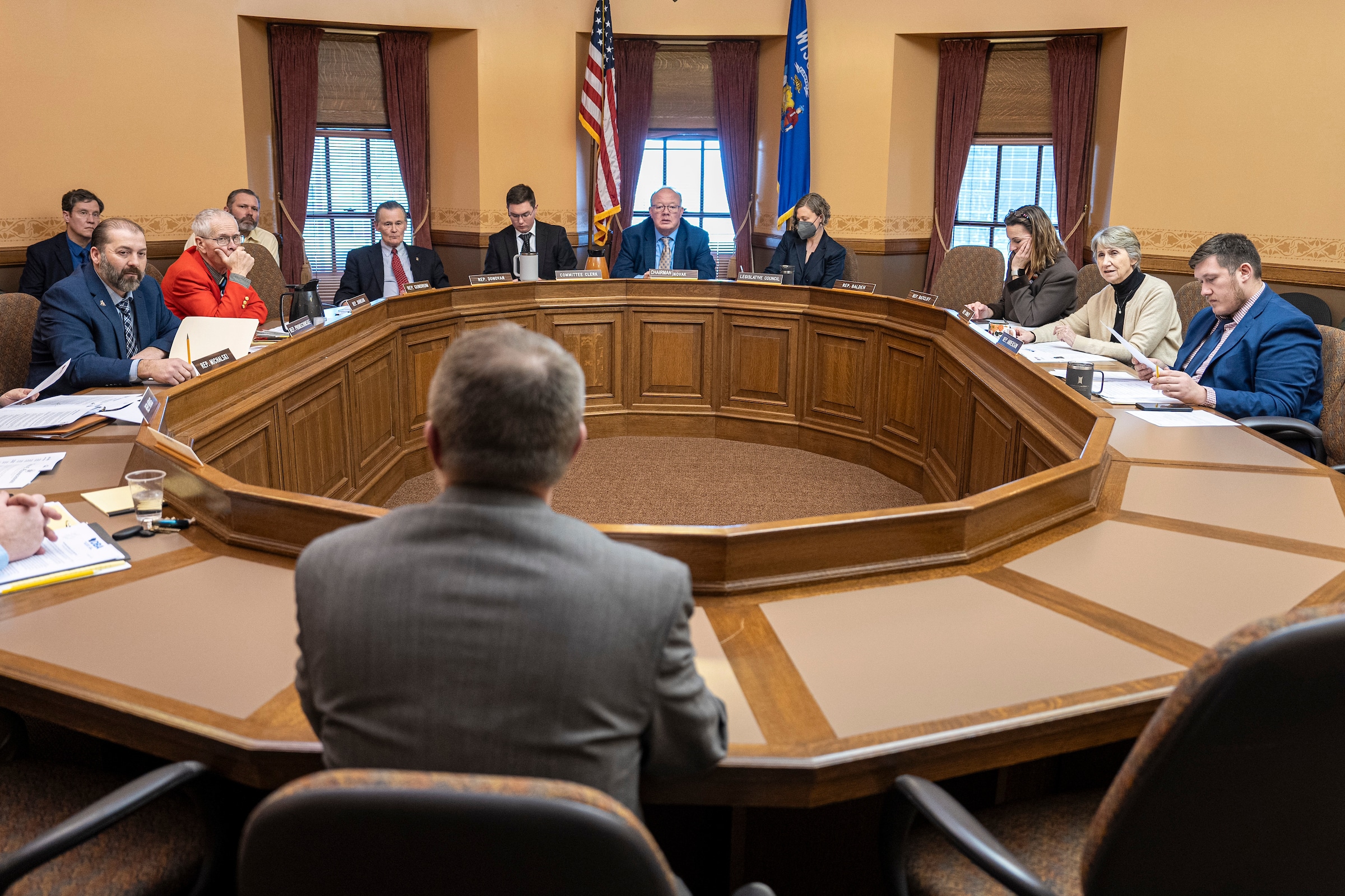 ||Rep. Treig Pronschinske speaks at a committee hearing.|Any Marshall stands outdoors with trees in the background.|Profile view of AV Roth speaking before the committee.