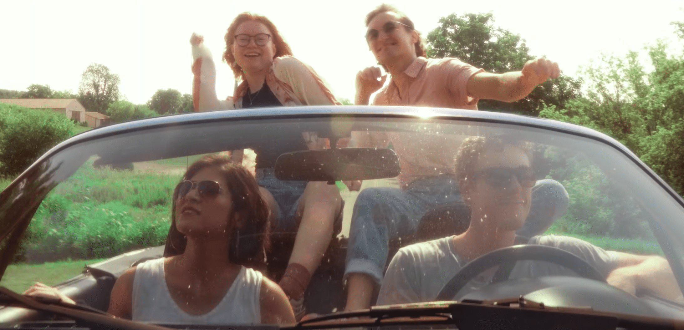 The four members of LINE are shown leaning against a blue convertible.