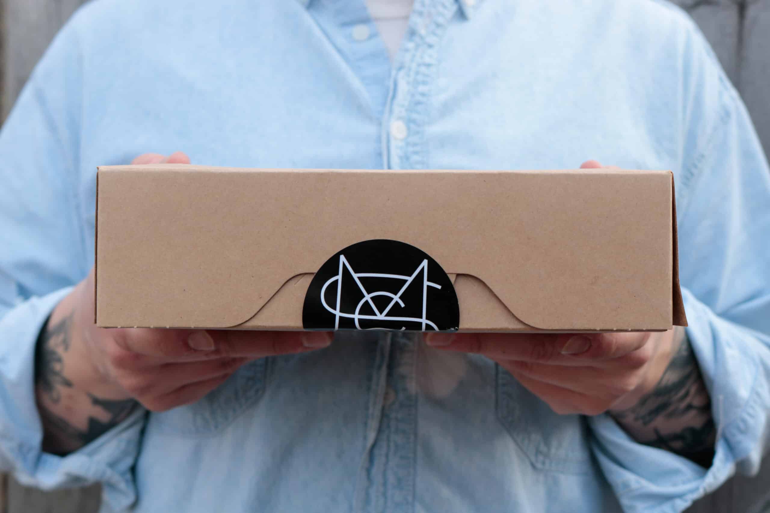A box of pastries, sealed with a sticker featuring the Madison Sourdough logo.|A selection of breads available displayed on wooden shelving at Madison Sourdough.|A Madison Sourdough delivery van, which is white with the Madison Sourdough logo on the back.