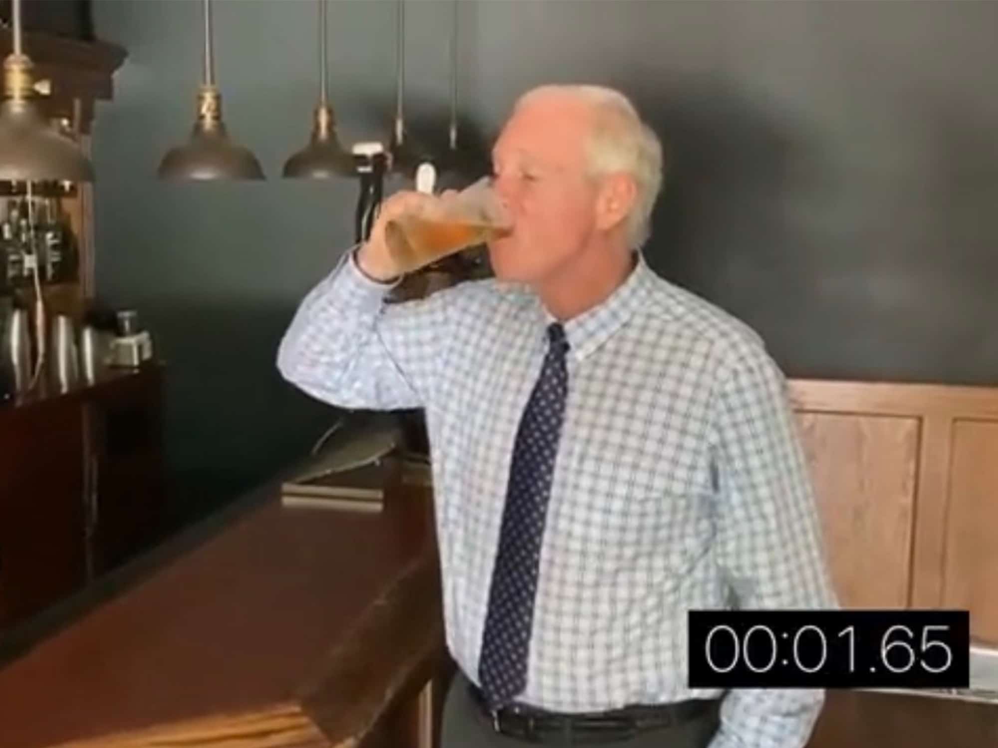 A screenshot from a video shows Senator Ron Johnson drinking a beer in a sad bland-looking bar. In the lower right-hand corner, a timer counts up how long it is taking him to drink the beer.