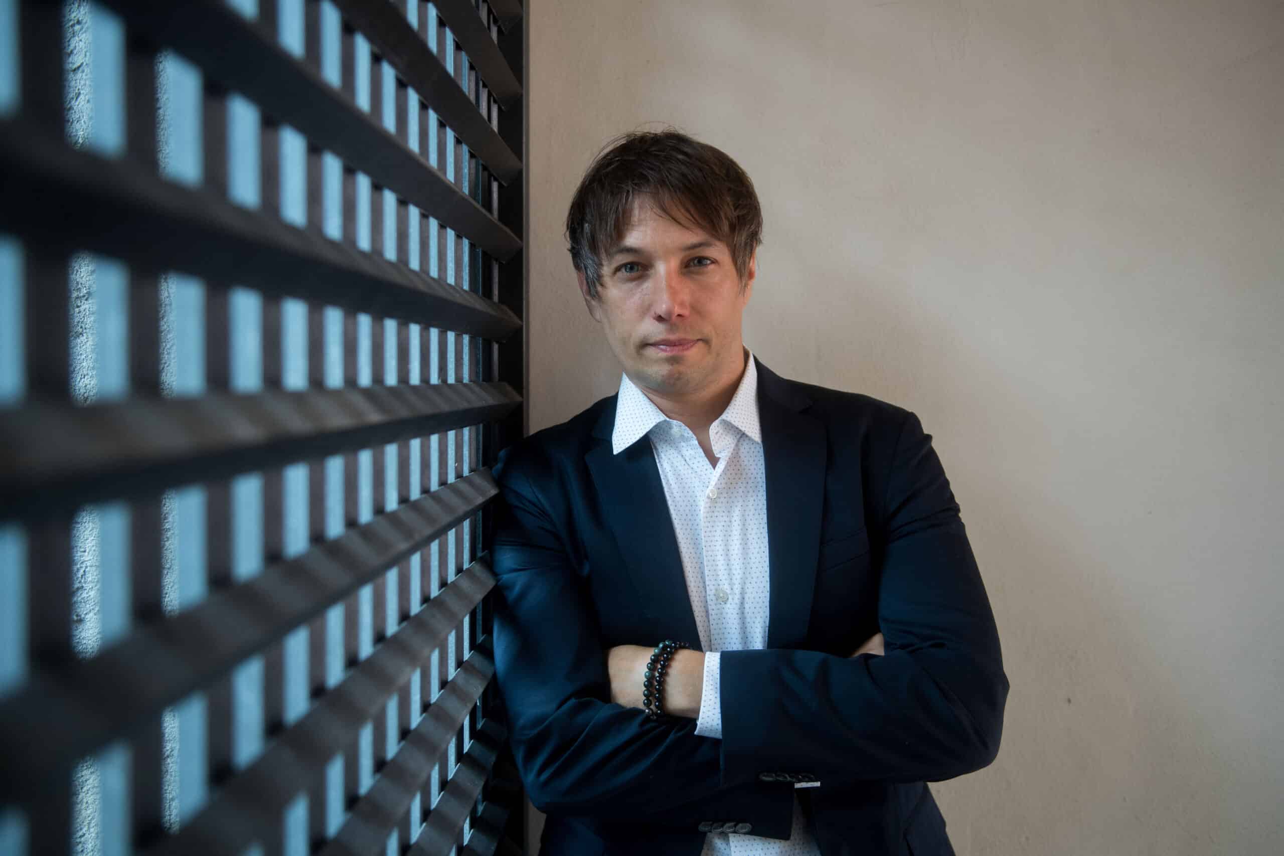 Writer-Director Sean Baker faces the camera with his arms crossed in a photo taken as a jury member at a past Locarno Film Festival. Photo by Samuel Golay.|A still from the film "Take Out" shows Ming Ding (Charles Jang) collecting payment for a food delivery at a Manhattan apartment building.