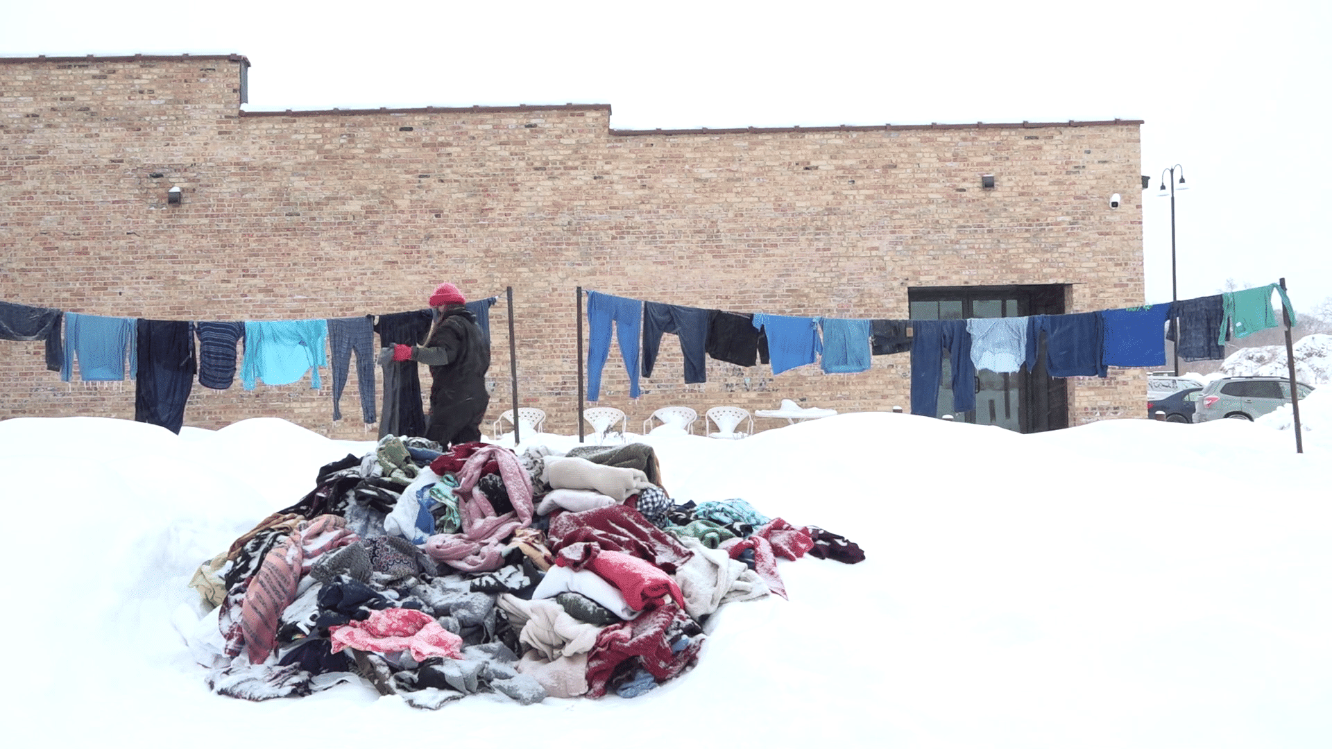 At Garver Feed Mill, artist Ray Carruthers hangs an assortment of blue garments on clotheslines in frigid conditions for the exhibit "Fashion Is Forever." In the foreground, a mound of differently colored balled-up clothing sprawls out in a mound of snow.|